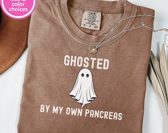 May include: A brown t-shirt with a distressed look featuring a white ghost and the text "GHOSTED BY MY OWN PANCREAS".