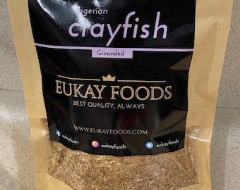 May include: A brown paper bag with a black label that says "Nigerian Crayfish Grounded" and "EUKAY FOODS BEST QUALITY, ALWAYS!" with a website address and social media icons. The bag contains a brown powder.