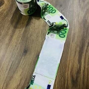 May include: A roll of fake money, resembling a toilet paper roll, with 100 euro bills wrapped around a white cardboard core.