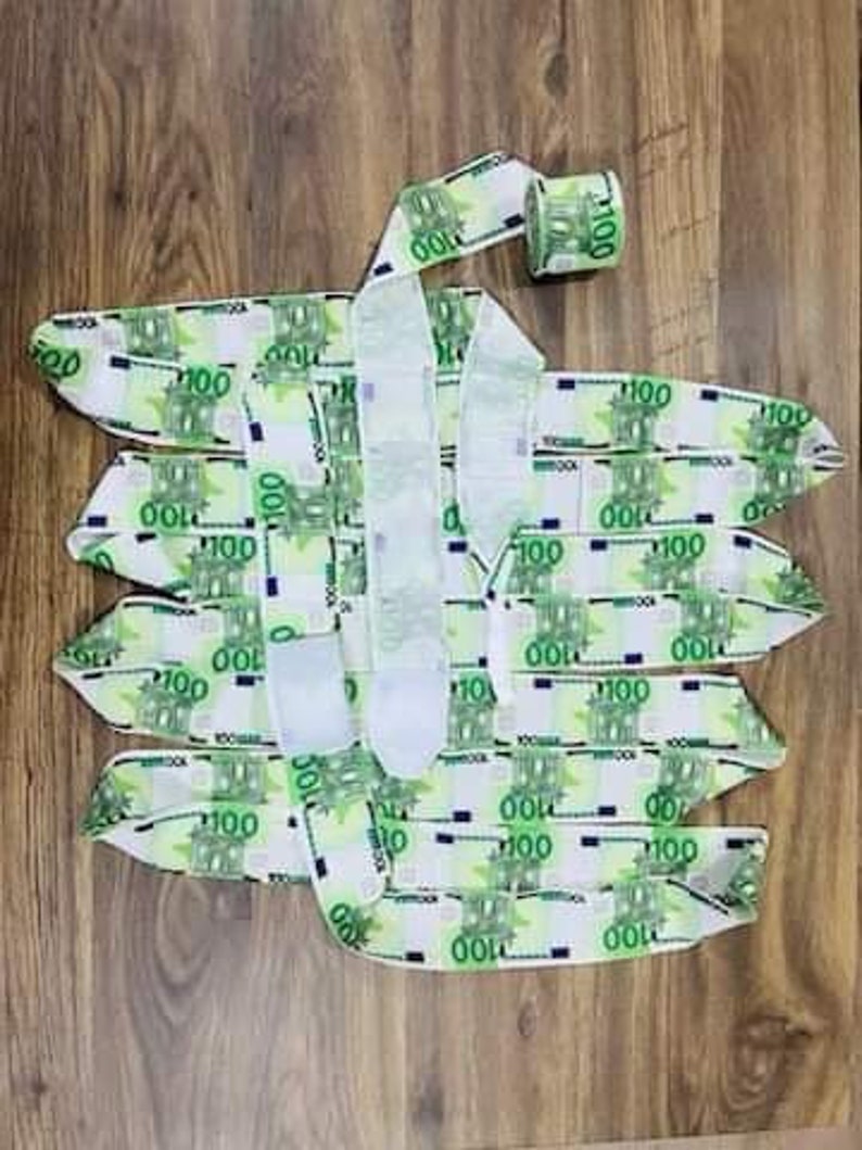 May include: A roll of white ribbon with a repeating pattern of 100 Euro bills. The ribbon is unrolled and folded in a decorative way.