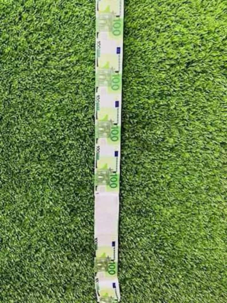 May include: A long strip of paper with images of 100 Euro bills printed on it. The paper is white with a green background and the bills are printed in blue and green.