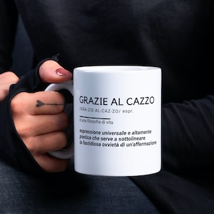 May include: White ceramic mug with black text that reads "GRAZIE AL CAZZO /GRA-ZIE-AL-CAZ-ZO/ espr. è una filosofia di vita espressione universale e altamente poetica che serve a sottolineare la fastidiosa ovvietà di un'affermazione"