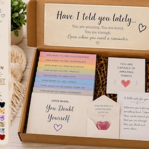 May include: A brown cardboard gift box containing twenty colorful envelopes labeled with various prompts like Open When You Need Encouragement. The box includes a small pink heart-shaped gem, printed cards with motivational text, and a list of contents.