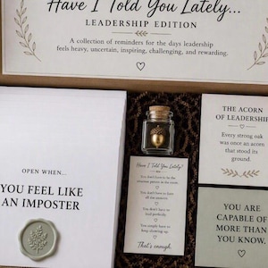 May include: A cardboard gift box titled Have I Told You Lately... Leadership Edition containing white envelopes with wax seals, a small glass jar with a gold acorn, and several printed cards with motivational text about leadership and personal growth.