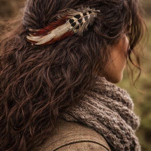 May include: A decorative feather hair clip with brown, red, and black markings is placed in dark brown wavy hair. The person is wearing a brown jacket and a gray knitted scarf.