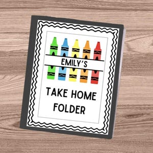May include: A personalized take-home folder with a black border and a white interior. The folder features a crayon design in various colors, with the name "Emily's" above the text "Take Home Folder". The background is a light brown wood grain.