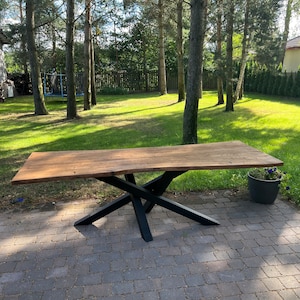 Può includere: Un lungo tavolo in legno con un piano in legno vivo e una base a X in metallo nero. Il tavolo è posizionato su un patio in mattoni.