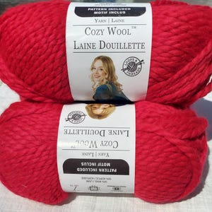 May include: Two large balls of red Cozy Wool yarn. Each ball has a white label with the text "Cozy Wool" and "Laine Douillette". The labels also feature a woman's portrait and the words "Pattern Included".