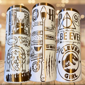 May include: Three white cylindrical tumblers featuring metallic gold illustrations of various literary and cinematic icons, including a wardrobe, a lamp post, a wizard, a dinosaur, the Deathly Hallows symbol, and text such as Never Grow Up and Clever Girl.