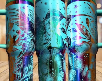 May include: Three cylindrical tumblers with handles and light blue lids. The tumblers feature a vibrant iridescent finish with a metallic hummingbird and floral pattern in shades of purple, gold, and blue. The design includes small dots and flowers.