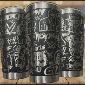 May include: A matte black stainless steel tumbler featuring laser-engraved graphics of professional wrestlers, including Hulk Hogan, The Rock, Hitman, and Rey Mysterio, alongside WWE and WWF logos and various wrestler names in a repeating pattern.