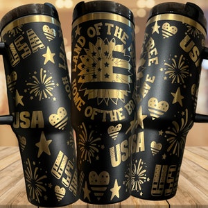 May include: Three black travel mugs with gold lettering and designs. The mugs feature patriotic themes with the words "Land of the Free", "Home of the Brave", and "USA".