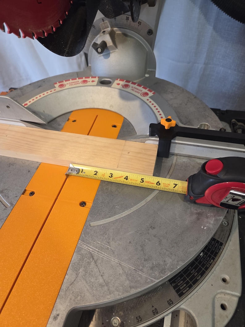 May include: A miter saw with a wooden plank and a measuring tape. The saw has a red blade and orange supports. The tape measure shows a measurement of approximately 6 inches.