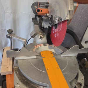 May include: A silver and orange miter saw with a red blade. The saw has a clear blade guard and an orange safety guard. The saw is designed for cutting wood and other materials.