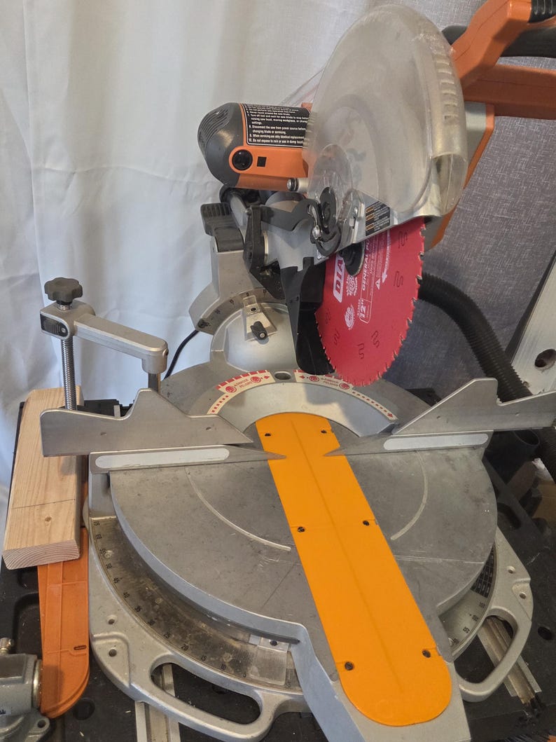 May include: A silver and orange miter saw with a red blade. The saw has a clear blade guard and an orange safety guard. The saw is designed for cutting wood and other materials.
