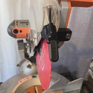 May include: A power miter saw with a red blade and orange and gray accents. The saw has a clear plastic blade guard and a black handle. The saw is designed for cutting wood and other materials.