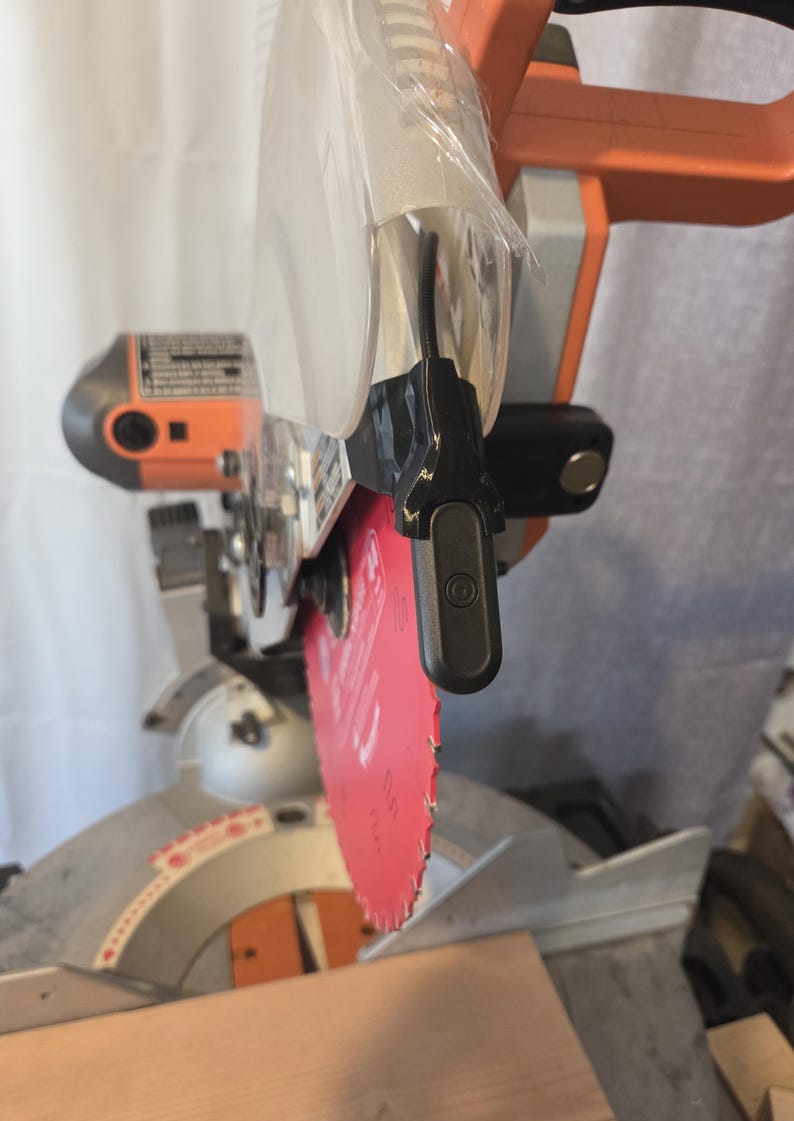 May include: A power miter saw with a red blade and orange and gray accents. The saw has a clear plastic blade guard and a black handle. The saw is designed for cutting wood and other materials.