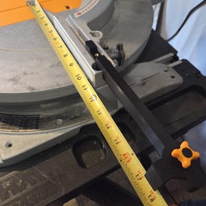 May include: A miter saw with a yellow measuring tape extended across the blade. The saw is gray and black with an orange accent. The tape shows measurements up to 19 inches.