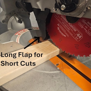 K&ouml;nnte beinhalten: Eine Gehrungss&auml;ge mit einem roten S&auml;geblatt schneidet ein Holzst&uuml;ck. Der Text "Long Flap for Short Cuts" ist sichtbar. Das S&auml;geblatt hat 44 Z&auml;hne und ist f&uuml;r pr&auml;zise, saubere Schnitte ausgelegt. F&uuml;r 12" Gehrungs- und Schiebemeters&auml;gen.