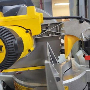 Puede incluir: Primer plano de una herramienta eléctrica amarilla y negra con un protector de cuchilla plateado. La herramienta tiene un mango negro y una carcasa de motor amarilla con la palabra "WALT" impresa en ella.