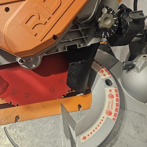 K&ouml;nnte beinhalten: Eine orangefarbene und graue Gehrungss&auml;ge mit rotem S&auml;geblatt. Auf dem orangefarbenen Geh&auml;use ist der Markenname "RIDGID" eingepr&auml;gt. Der Klingenschutz tr&auml;gt einen Warnhinweis "DANGER PELIGRO".