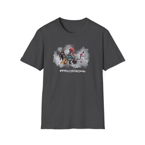 May include: Dark gray t-shirt with a graphic of Philadelphia athletes in a cloud of smoke. The text '#PHILLYSTRONG' is printed below the graphic.