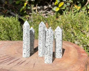 May include: Six white and gray granite crystal points arranged in a semi-circle on a wooden surface. The points are all about the same size and have a speckled appearance.