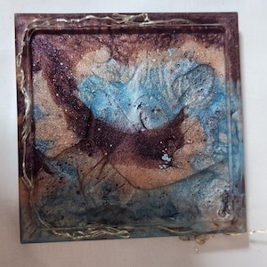 May include: Square resin coaster with a blue, brown, and beige marbled design. The coaster has a clear resin border.