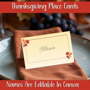 Puede incluir: Tarjeta de mesa de Acción de Gracias crema con el nombre "Alison" en letra cursiva. Tiene un borde marrón y detalles de hojas de otoño. La tarjeta está sobre una servilleta color óxido. El texto dice "Names Are Editable In Canva".