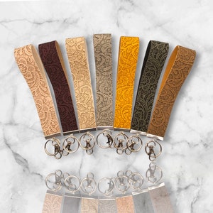 May include: Set of eight keychains with different colored leather straps and intricate lace patterns. Each keychain has a silver key ring.