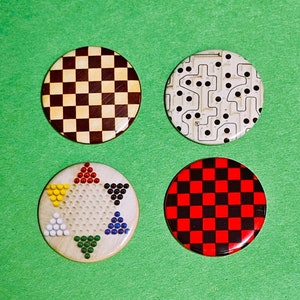 May include: Four round game pieces with different designs on a green background. One piece has a brown and beige checkerboard pattern, another has a black and white pattern, a third has a Chinese checkers design, and the last has a red and black checkerboard pattern.