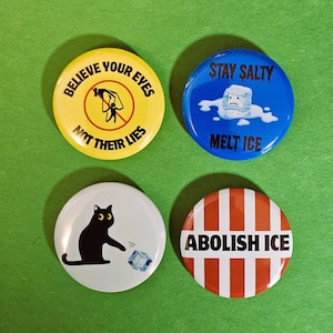 以下が含まれることがあります： さまざまなデザインの丸いピンバッジが4つ。黄色のボタンには「Believe Your Eyes Not Their Lies」と書かれています。青いボタンには「Stay Salty Melt Ice」と書かれています。白いボタンには黒猫と氷の塊が描かれています。赤と白のストライプのボタンには「Abolish Ice」と書かれています。