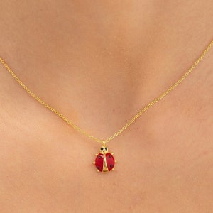 May include: A gold chain necklace with a red ladybug pendant. The ladybug has black spots and gold accents.