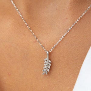 Può includere: Una collana con catena d'argento con un piccolo ciondolo delicato a forma di foglia con pietre di zircone cubico trasparenti.