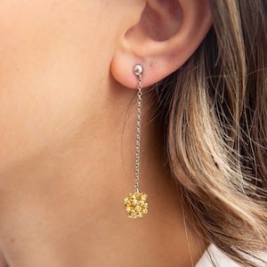 May include: A pair of gold and silver dangle earrings with a small ball at the top and a larger ball at the bottom. The larger ball is made of many small gold beads.