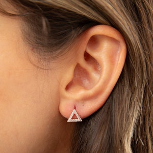 May include: A pair of small, silver triangle earrings with clear cubic zirconia stones set in the outline of the triangle.