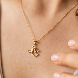 May include: A gold chain necklace with a delicate angel pendant. The angel is holding a small heart in its hand.