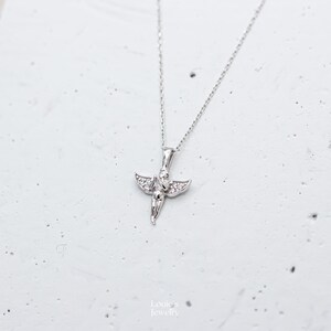 Pu&ograve; includere: Una collana d'argento con un piccolo ciondolo a forma di angelo decorato con pietre di zircone cubico trasparenti.