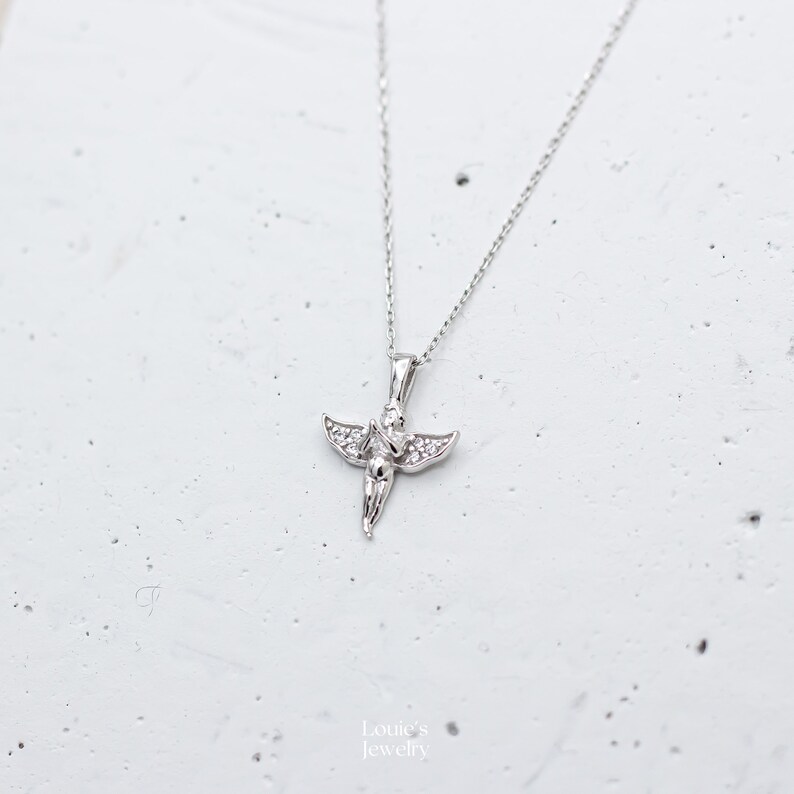 Pu&ograve; includere: Una collana d'argento con un piccolo ciondolo a forma di angelo decorato con pietre di zircone cubico trasparenti.