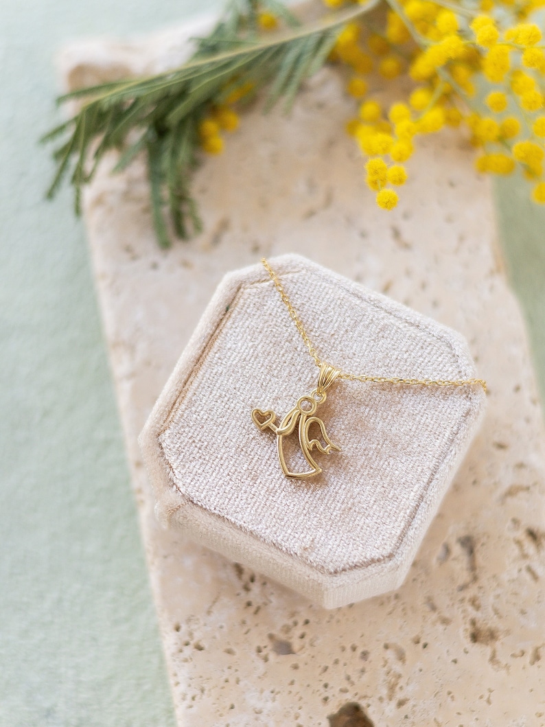 May include: A gold angel pendant necklace with a heart detail, displayed in a white velvet box.