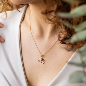 May include: A gold chain necklace with a delicate angel pendant. The angel is holding a small heart in its hand.