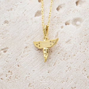 Pu&ograve; includere: Una collana con un ciondolo a forma di angelo in oro, decorato con piccole pietre trasparenti sulle ali. Il ciondolo &egrave; su una delicata catena d'oro.