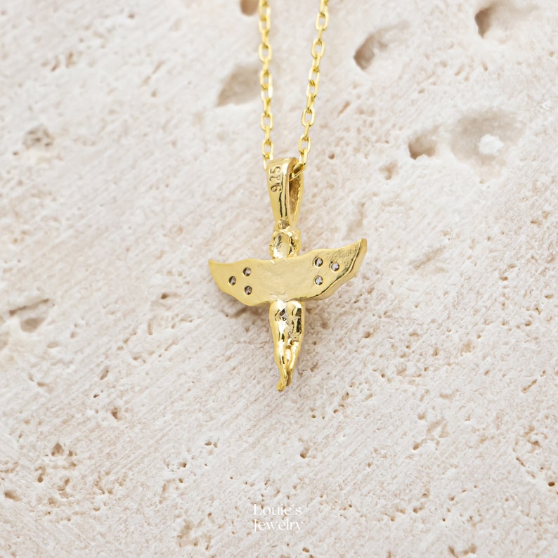 Pu&ograve; includere: Una collana con un ciondolo a forma di angelo in oro, decorato con piccole pietre trasparenti sulle ali. Il ciondolo &egrave; su una delicata catena d'oro.