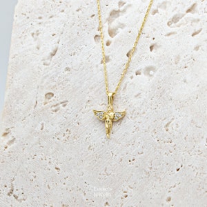 Pu&ograve; includere: Una collana con catena dorata con un piccolo ciondolo a forma di angelo decorato con pietre di zircone cubico trasparenti.