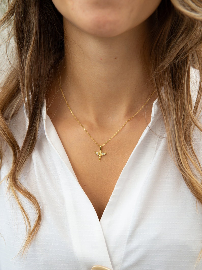 Pu&ograve; includere: Una collana con catena dorata con un piccolo ciondolo a forma di angelo con pietre di zircone cubico trasparenti.