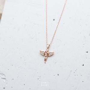 Pu&ograve; includere: Una collana in oro rosa con un piccolo ciondolo a forma di angelo decorato con pietre di zircone cubico trasparenti.