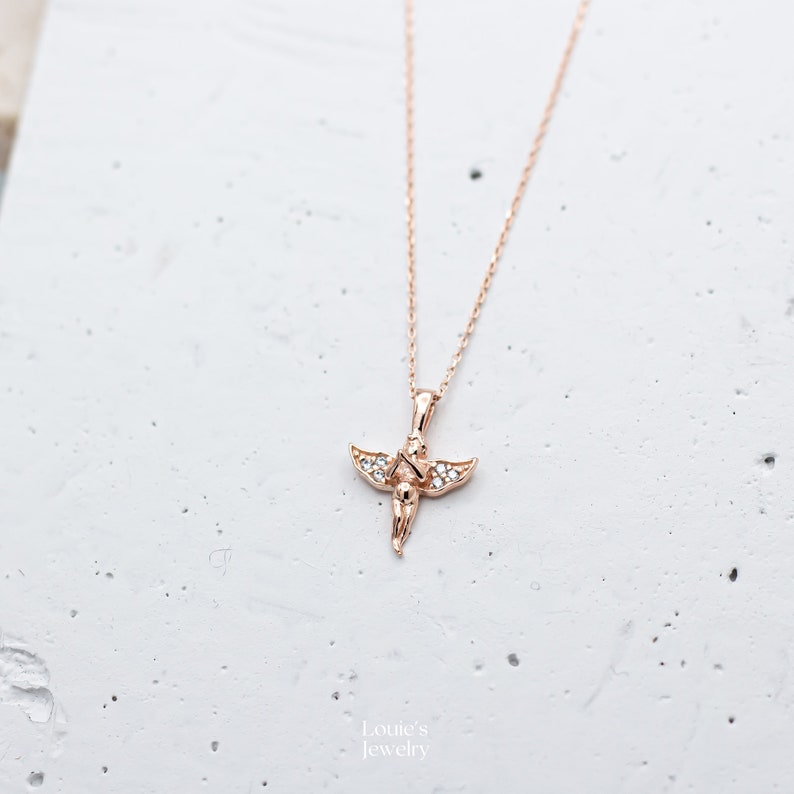 Pu&ograve; includere: Una collana in oro rosa con un piccolo ciondolo a forma di angelo decorato con pietre di zircone cubico trasparenti.