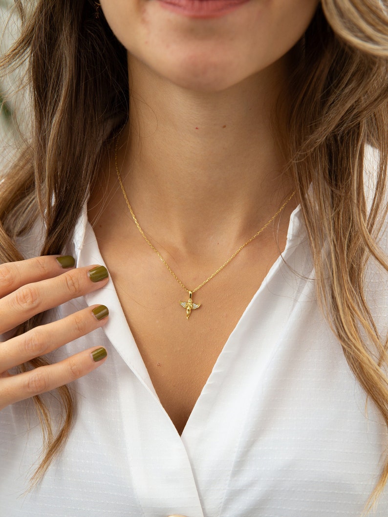 Pu&ograve; includere: Una collana con catena d'oro con un piccolo ciondolo a forma di angelo. L'angelo ha le ali e un'aureola.