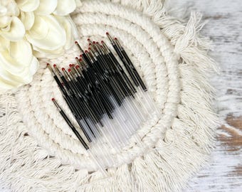 May include: A bunch of black and clear pens with red tips are arranged in a circle on a white crocheted coaster with fringe.