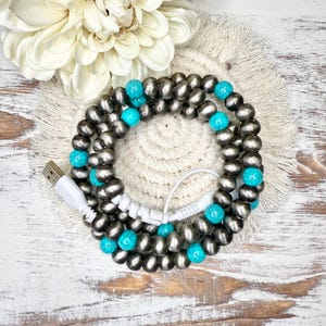 May include: A silver and turquoise beaded phone charging cable wrapped around a white cord.